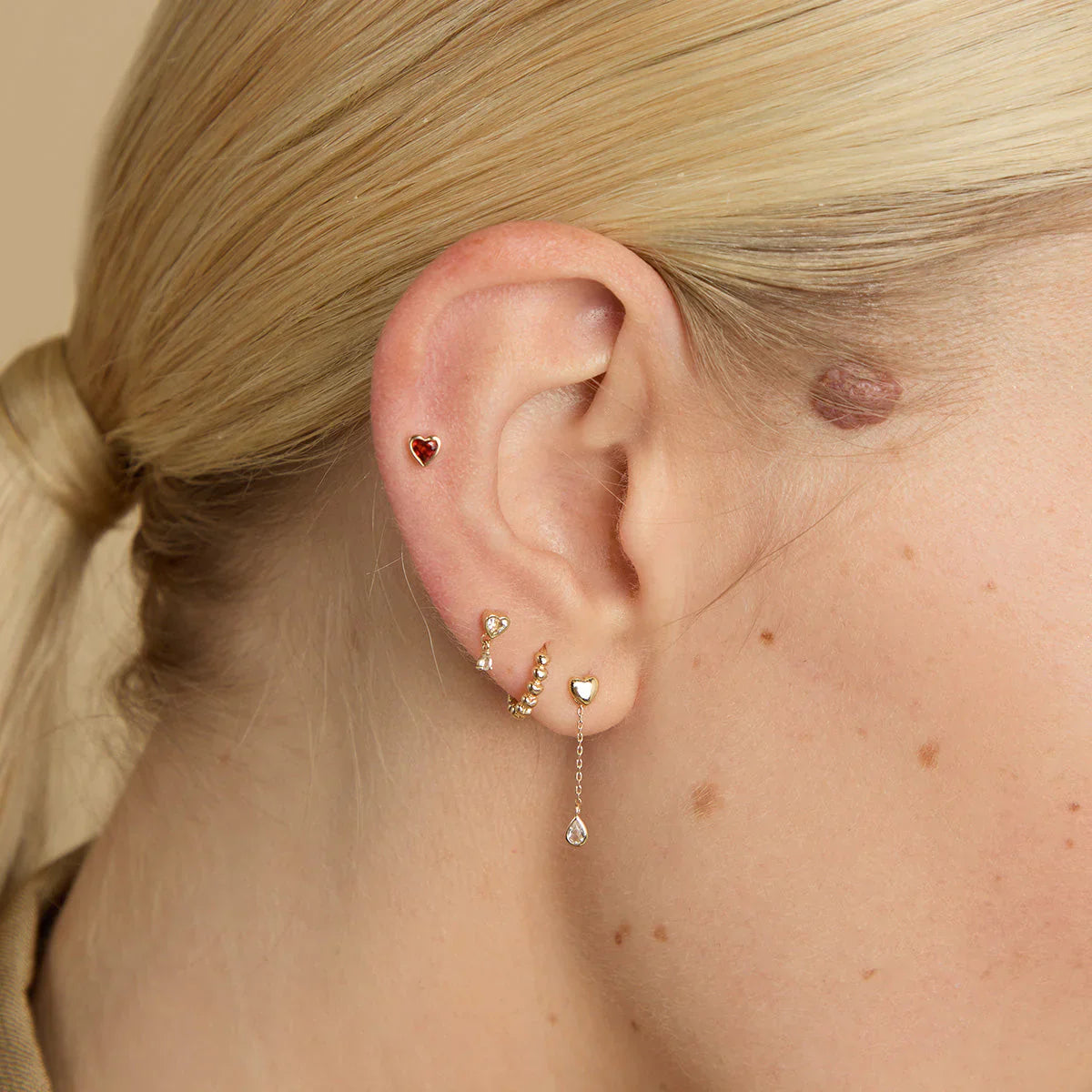 Woman wearing solid gold daith earrings stacked with other solid gold piercing jewellery on her right ear.