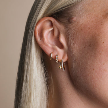 Side profile of a woman wearing matching Astrid & Miyu crystal huggies and ear cuffs in gold.