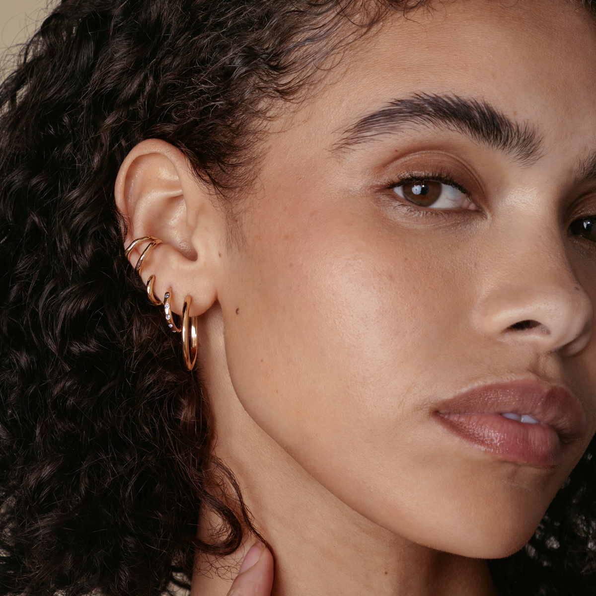 Side profile of a woman wearing matching Astrid & Miyu crystal huggies and ear cuffs in gold.