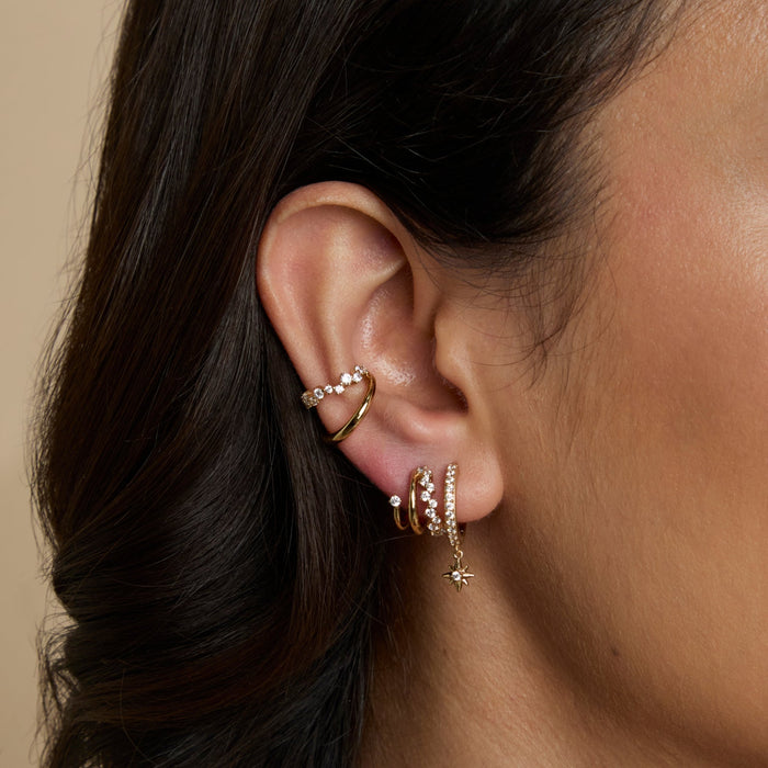 Side profile of a woman wearing matching Astrid & Miyu crystal huggies and ear cuffs in gold.