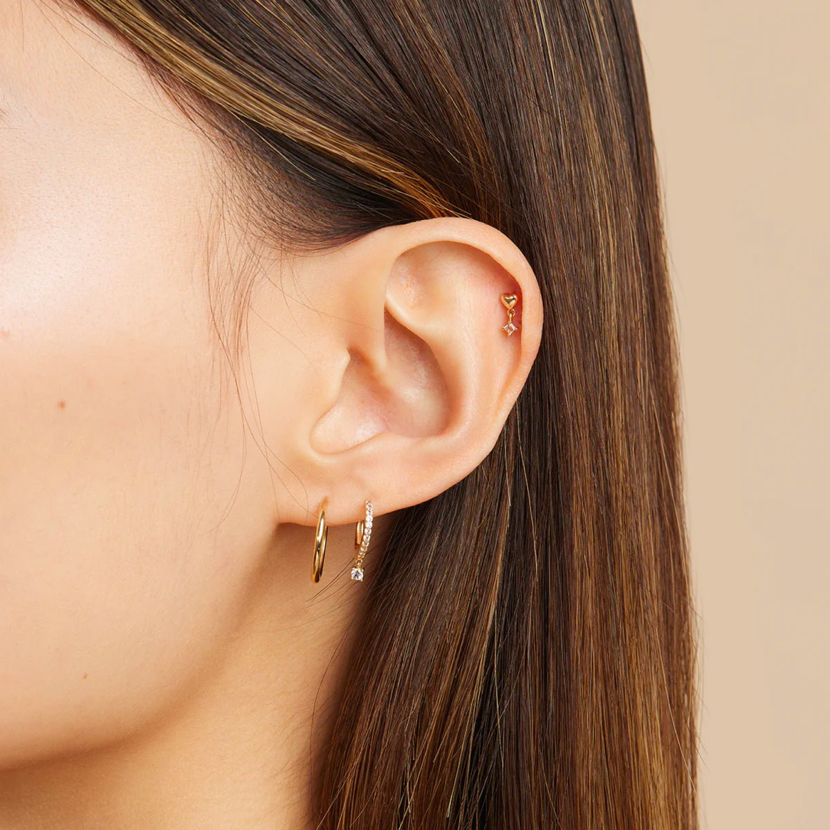 Woman wearing solid gold daith earrings stacked with other solid gold piercing jewellery on her right ear.